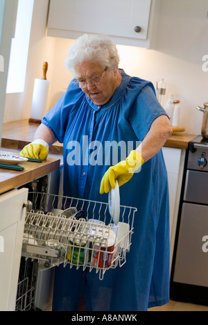 Unabhängige ältere Seniorin allein, selbstständige Witwe, die ihren Geschirrspüler in ihre moderne, sichere Hausküche lädt Stockfoto