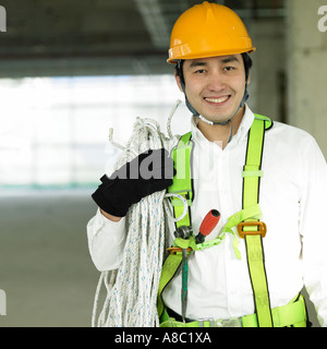 Legen Sie beim Bau eines Arbeitnehmers mit einem Seil auf der Schulter Stockfoto