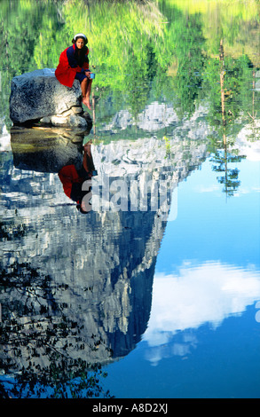 Yosemite-Nationalpark, Sierra Nevada, USA. Junge Frau Wanderer sitzt auf Felsen in Mirror Lake in Merced River. Half Dome hinter Stockfoto