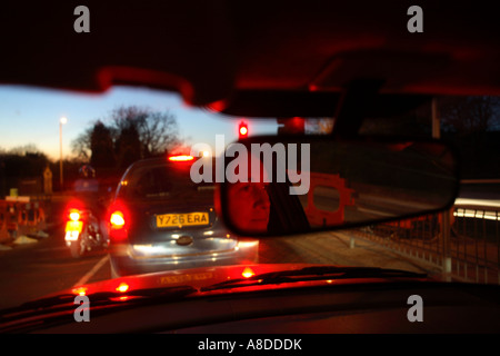 Eine Fahrerin ist durchschaut ihr Rückspiegel bei der Aufwartung an einer roten Ampel im ruhenden Verkehr in Süd-London-UK Stockfoto