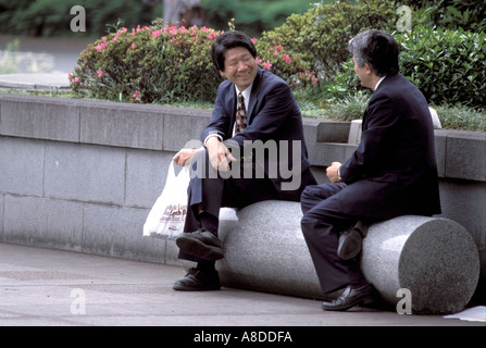 Zwei Angestellte oder Angestellte Büroangestellte oder Geschäftsleute sitzen während ihrer Mittagspause im Wadakura Fountain Park im Herzen von Tokio, Japan. Stockfoto