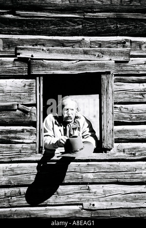 Ein Cowboy im Fenster eine rustikale Hütte mit seinem Hut ab Stockfoto