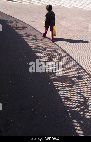 Eine Person geht entlang ein Schatten des Zauns mit geparkten öffentliche Fahrräder auf den Haag Holland Stockfoto