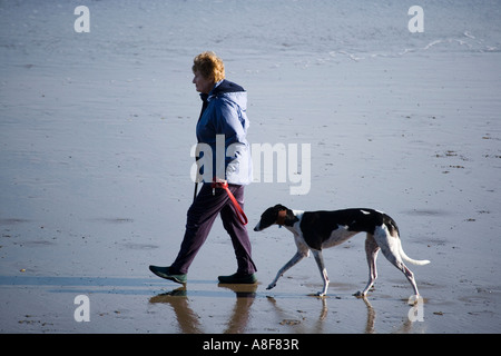 Frau am Strand zu Fuß mit ihrem Hund an der Leine Stockfoto