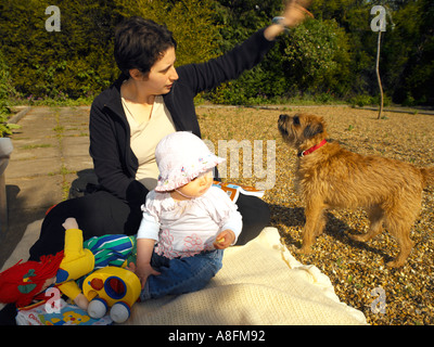 Mutter mit acht Monate altes Baby Mädchen Border Terrier spielen im Garten Stockfoto