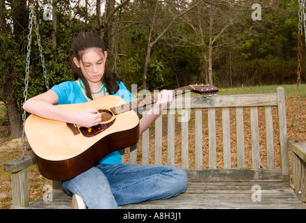 Teen Mädchen zwischen 13 und 15 Jahren, die einen sonnigen Tag genießen, während sie auf einer Schaukel im Freien sitzen und Gitarre spielen. USA Stockfoto