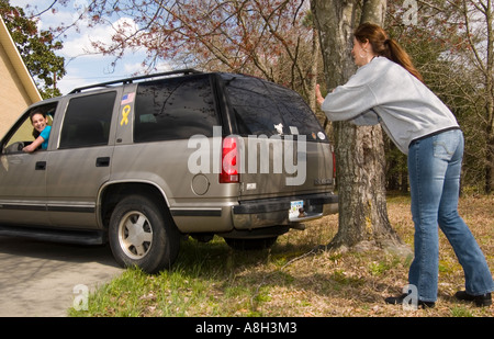 Teenager-Mädchen fährt Auto, während ihre besorgte Mutter in der Nähe in den USA steht. Stockfoto