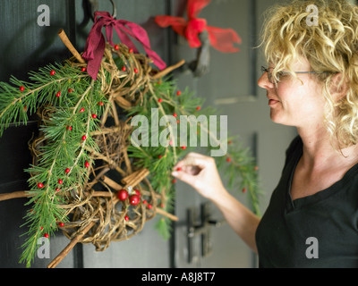 junge Frau putzt die vordere Tür mit Kranz Dekoration Weihnachten Gäste vorbereiten Stockfoto