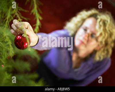 Person putzt den Weihnachtsbaum mit einer roten Kugel Dekoration erschossen von oben Stockfoto