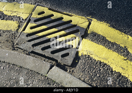 Detail von oben der frisch gestrichene doppelte gelbe Linien einer Kurve in der Straße folgt und ein Abfluss Raster überfahren Stockfoto