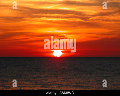 Schöne Feuer wie Sonnenuntergang am Coquina Beach mit kleinen Segelschiff am Horizont Florida USA Stockfoto