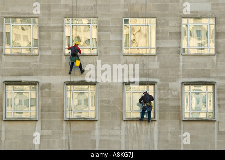 Horizontale Porträt von zwei Fensterputzer aus Seilen hoch oben auf einem Bürogebäude ausgesetzt. Stockfoto