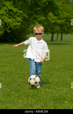 Vertikale Porträt eines jungen Mannes (4 Jahre alt) treten einen Fußball während eines Spiels in den Park in eine Frühlingssonne. Stockfoto