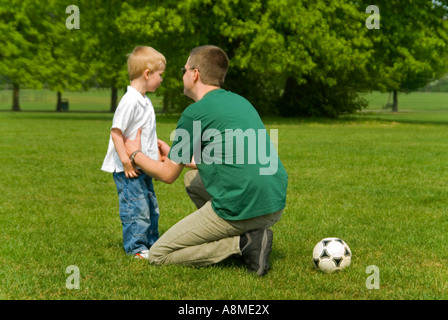 Horizontale Porträt eines jungen Vaters Disziplinierung seinen jungen Sohn während eines Spiels der Fußball im park Stockfoto