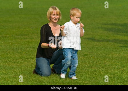 Horizontale Porträt einer jungen kaukasischen Mutter und ihrem kleinen Sohn Kommissionierung Löwenzahn Uhren in einem park Stockfoto