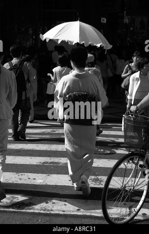 Eine Frau trägt einen traditionellen japanischen Kimono mit einem Sonnenschirm überquert eine Straße in Shinsaibashi-Osaka Japan Stockfoto