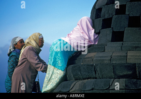 Frauen in traditioneller Kleidung, die versuchen, die Buddha-Statue in einem Stupa im Tempel von Borobudur, Indonesien versteckt zu erreichen Stockfoto