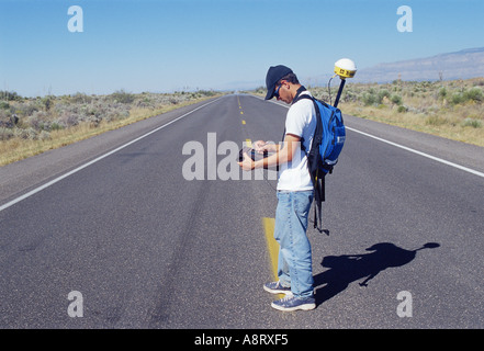 Junger Mann Vermessung einer einsamen Straße mit seinem Global Positioning System GPS-Gerät Stockfoto