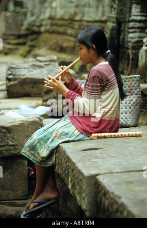 Khmer Mädchen Flötenspiel sitzt auf einer Mauer im Ta Prohm Tempel, Kambodscha Stockfoto