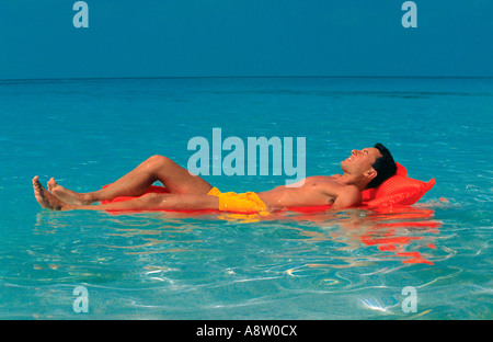 Malediven. Junger Mann in Badehose auf Luft Bett schwebend auf kristallklarem Wasser. Stockfoto