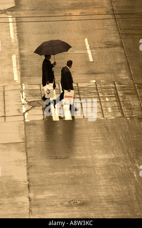 ZWEI MÄNNER IN ANZÜGEN WANDERN IN REGEN MIT REGENSCHIRM IN SEATTLE AUS KONFERENZ ÜBER KAFFEE TRAGEN TASCHEN VON TREFFEN Stockfoto