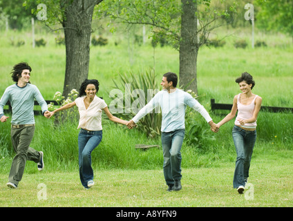 Vier junge Freunde Hand in Hand und im Feld überspringen Stockfoto