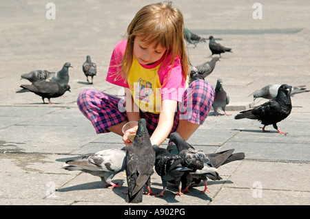 Horizontale Nahaufnahme eines jungen Mädchens hockend auf Futtermittel Tauben Samen aus der Handfläche von ihrer Hand an einem sonnigen Tag. Stockfoto