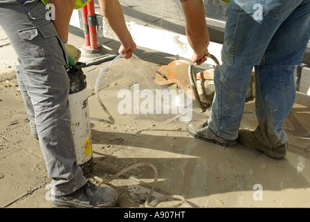 Rissige Pflaster Reparaturen Vermittlung in Arbeit zwei Arbeiter Scheibe schneiden Pflaster & Wasser Spray zu Dämpfen und Staub London England Großbritannien Stockfoto