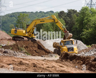 Mechanischen Bagger auf einer Bank, die Erde in einen LKW auf einer Straße, die Ausweitung der Regelung Köpfe der Täler Straße Wales UK ausgraben Stockfoto