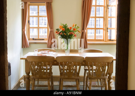 Ein Esszimmer in einem traditionellen Bauernhaus mit einem Holztisch und sechs Stühlen und eine Vase mit Blumen als Herzstück. Stockfoto