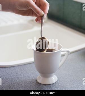 Machen eine schöne Tasse Tee. Vertikal genommen, ist eine Hand einen Teelöffel mit einen Teebeutel gegen die Innenseite des Bechers drauf. Stockfoto