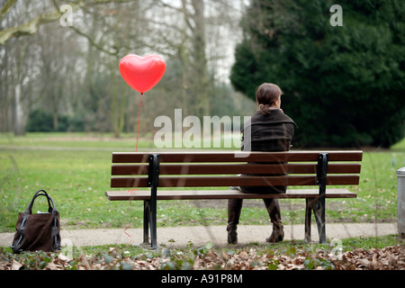 Eine junge Frau sitzt alleine auf einer Parkbank Stockfoto