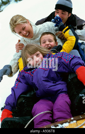 Eltern mit ihrem Sohn und Tochter einen Hügel hinunter auf einem Schlitten gleiten Stockfoto