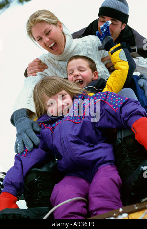 Eltern mit ihrem Sohn und Tochter einen Hügel hinunter auf einem Schlitten gleiten Stockfoto