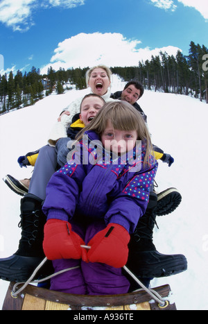 Eltern mit ihrem Sohn und Tochter einen Hügel hinunter auf einem Schlitten gleiten Stockfoto