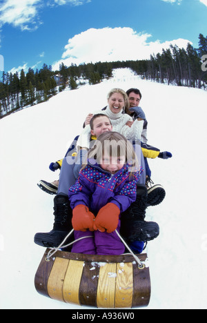 Eltern mit ihrem Sohn und Tochter einen Hügel hinunter auf einem Schlitten gleiten Stockfoto