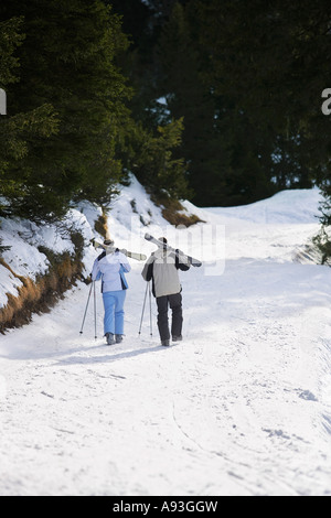 Ski Piste mit Skiern auf den Schultern hinunter paar Rückansicht, erhöhten Blick Stockfoto