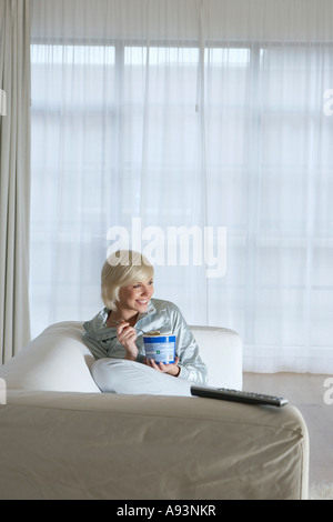 Frau sitzt auf dem Sofa, vor dem Fernseher und Eis essen Stockfoto