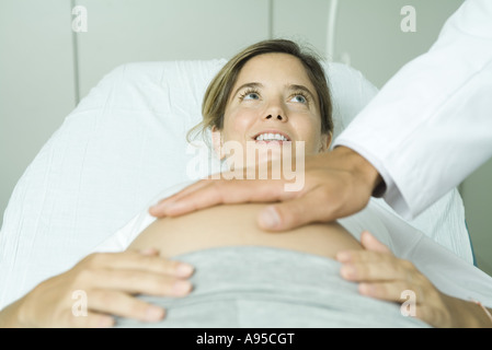 Schwangere Frau auf Rücken in Arztpraxis, ärztliche Hand auf Frau Bauch liegend Stockfoto