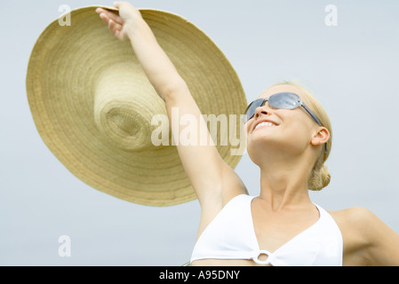 Junge Frau mit Sonnenbrille, Sonnenhut, Kopf und Schultern hochhalten Stockfoto