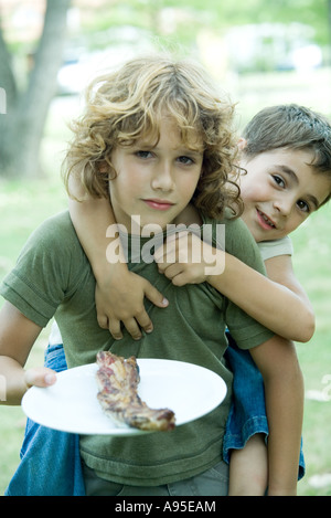 Junge hält gegrilltes Fleisch auf Teller, Freund Reiten Huckepack Stockfoto