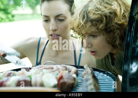 Familie mit Grillparty, Frau und Kind Blick auf Fleisch am Grill Grillen Stockfoto