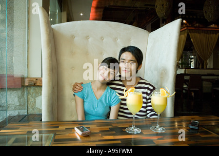 Junges Paar sitzt in Kabine, Cocktails am Tisch, lächelnd in die Kamera Stockfoto