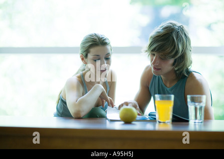 Junges Paar Ausübung Kleidung, sitzen nebeneinander, mit gesunden Snack und Blick auf Magazin Stockfoto
