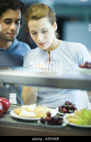 Two young adults standing, choosing healthy snack in cafeteria Stockfoto