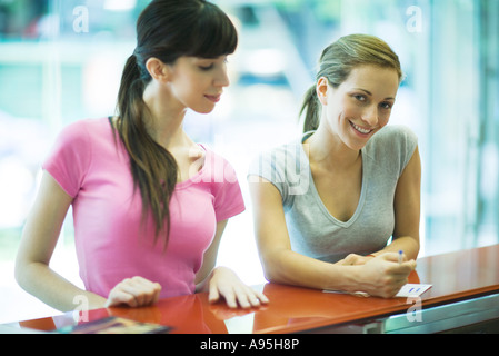 Zwei junge Frauen, die Check-in am Health Club Schalter, Hüfte aufwärts Stockfoto