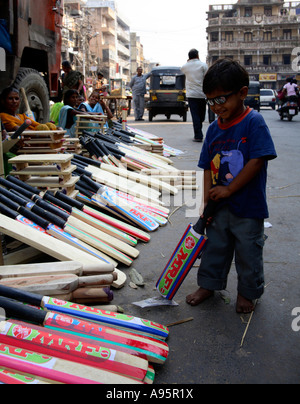 Kleiner Junge posiert neben Frauen verkaufen Kricketschläger an der Seite der Straße, Vadodara, Gujarat, Indien Stockfoto