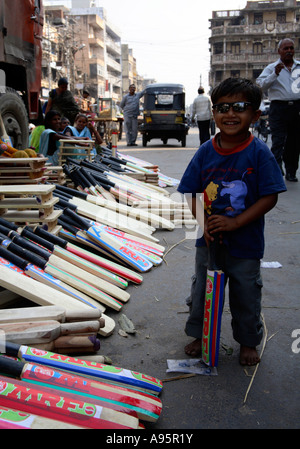 Junger indischer Junge posiert neben Frauen Verkauf Cricket Fledermäuse an der Seite der Straße, Vadodara, Gujarat, Indien Stockfoto