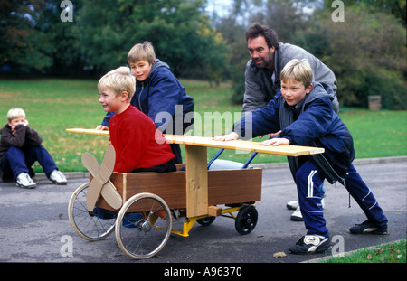 Ein Vater spielt mit seinen Söhnen und ihren hausgemachten Wagen im Park. Stockfoto