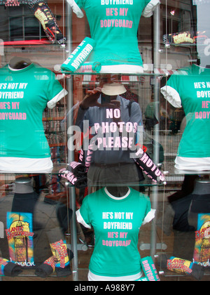 Funky T-Shirts in einem Londoner Schaufenster mit Reflexion der Fotograf Kamera mit Worten auf Hemd England halten Stockfoto